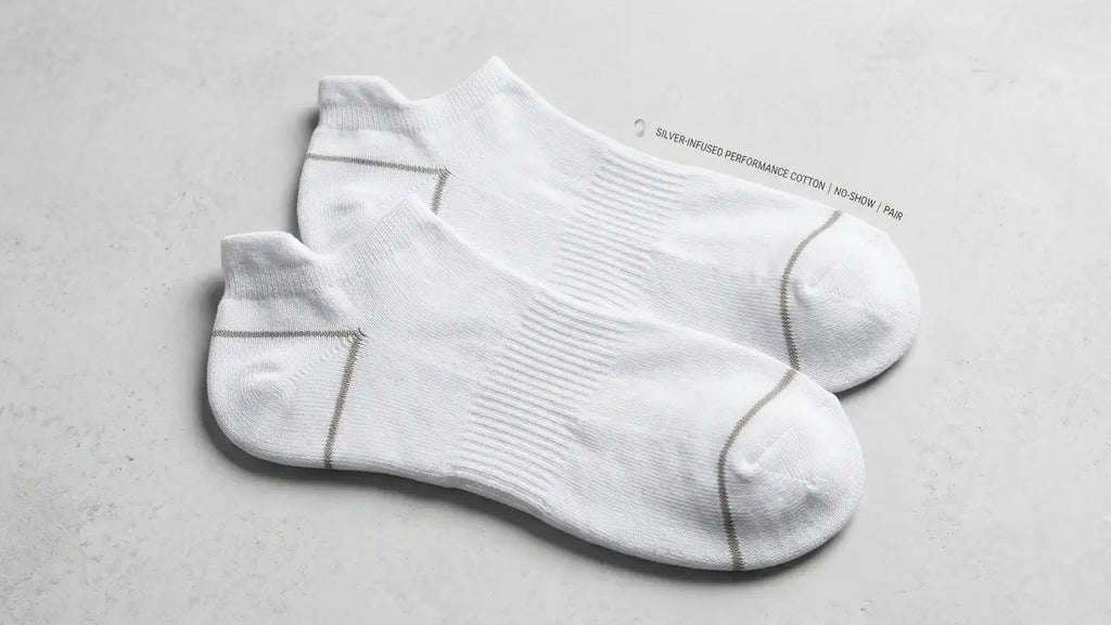 A pair of white low-cut athletic socks with gray contrast stitching, displayed on a light gray textured surface.
