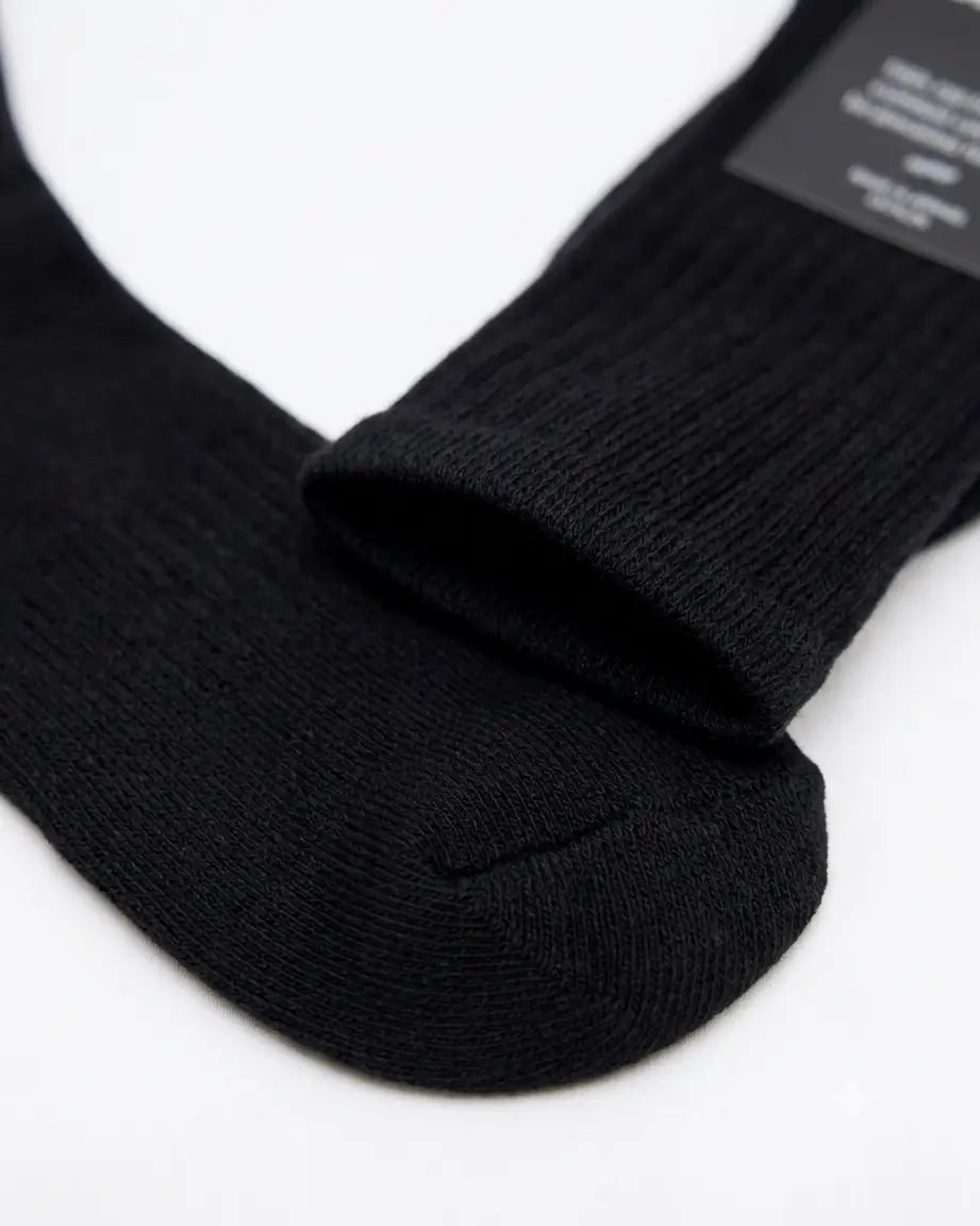 A close-up of a pair of black ribbed crew socks on a plain white background, with one sock folded over to show the ribbed texture and a small black product tag attached.