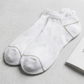 A pair of white low-cut ankle socks displayed next to their white packaging box and a small hangtag on a light gray textured background. Text in the upper right reads 'WHITE PROUD INDICS | PAIR PACK' with 'SILVER-INFUSED PERFORMANCE | PAIR PACK' below it.