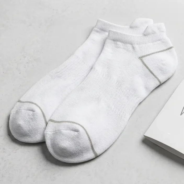 A pair of white low-cut ankle socks displayed next to their white packaging box and a small hangtag on a light gray textured background. Text in the upper right reads 'WHITE PROUD INDICS | PAIR PACK' with 'SILVER-INFUSED PERFORMANCE | PAIR PACK' below it.