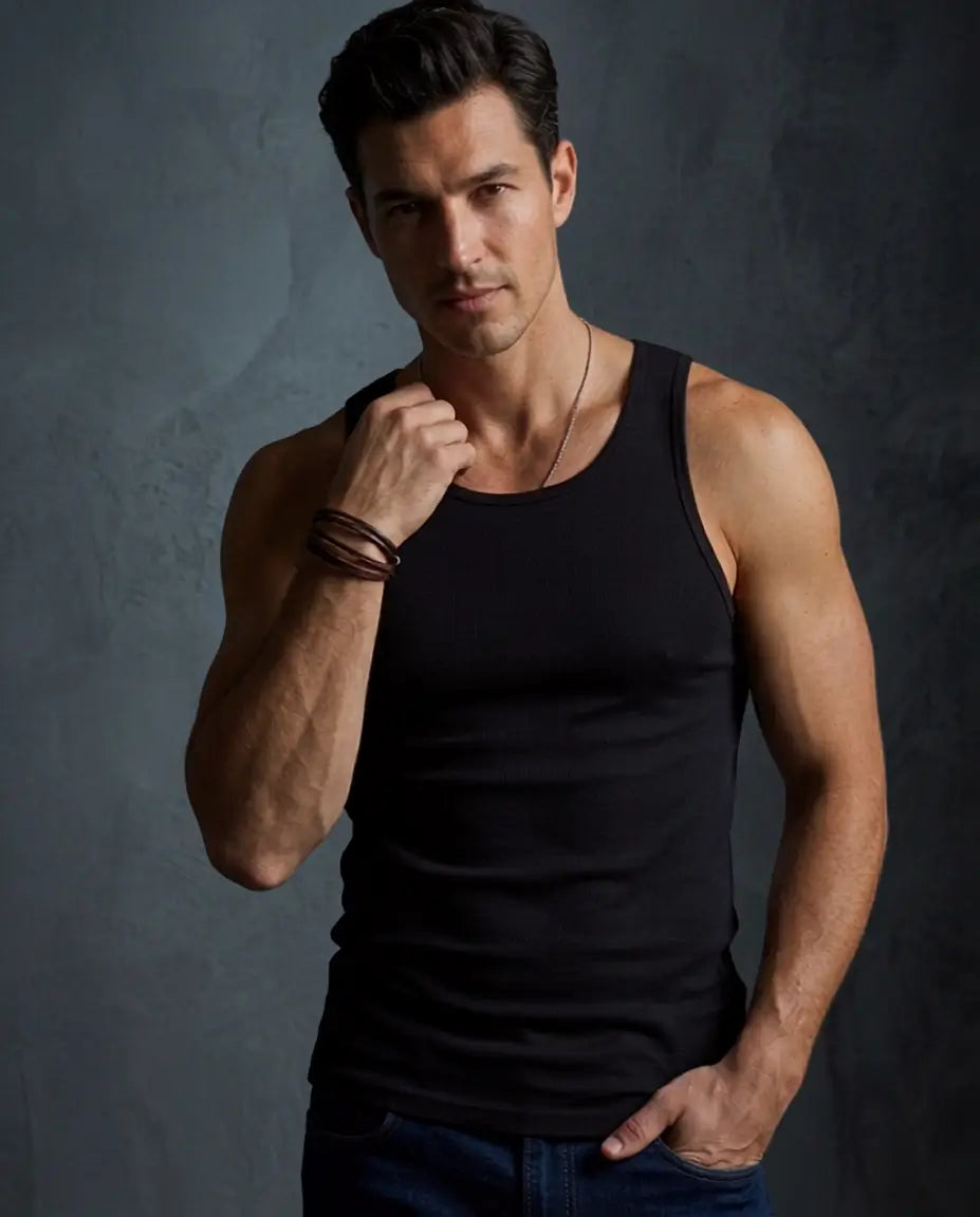 A muscular man wearing a black ribbed tank top and dark blue jeans, posing against a dark textured gray studio background.